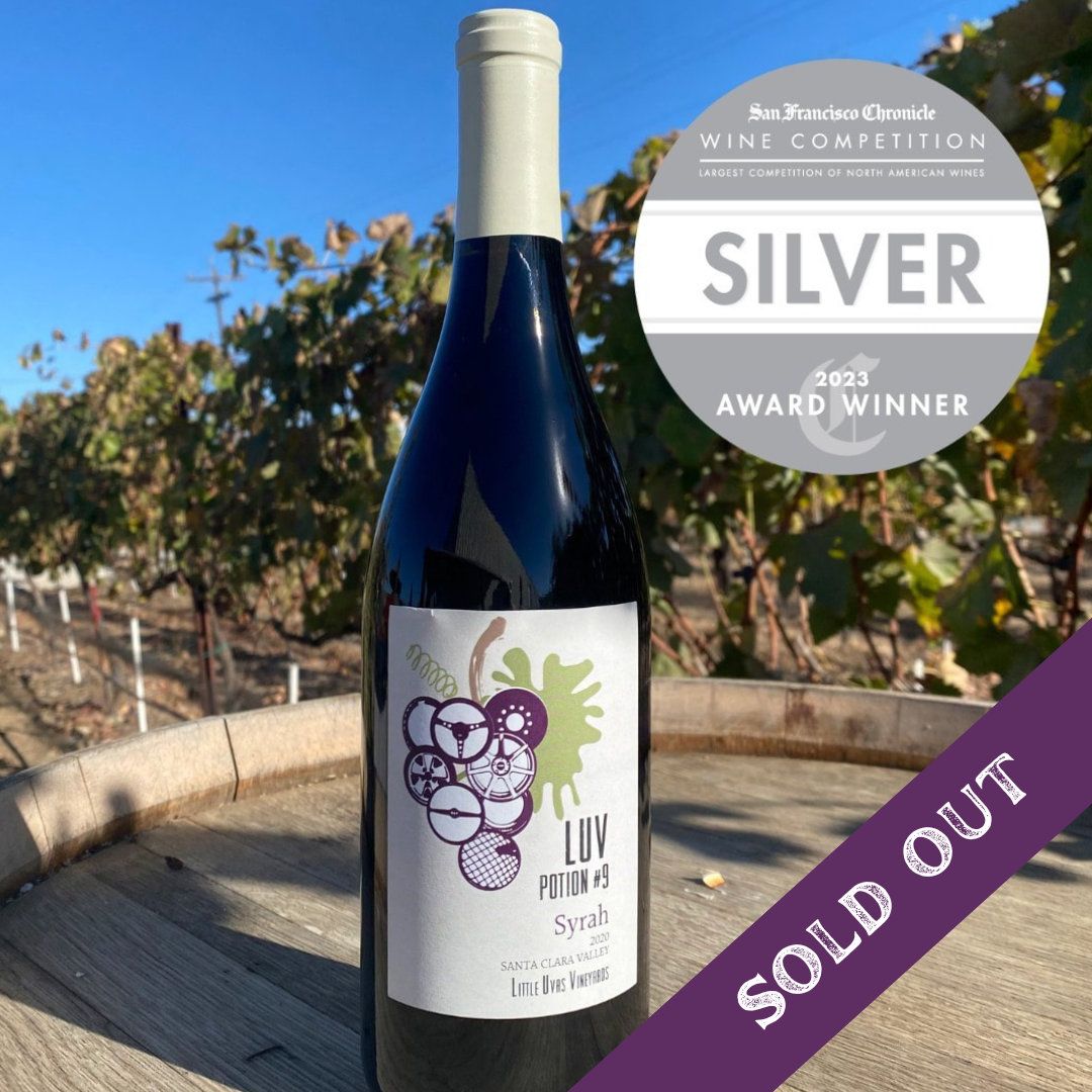 Sold Out bottle of LUV Syrah on a wine barrel with silver award badge and vineyard in background