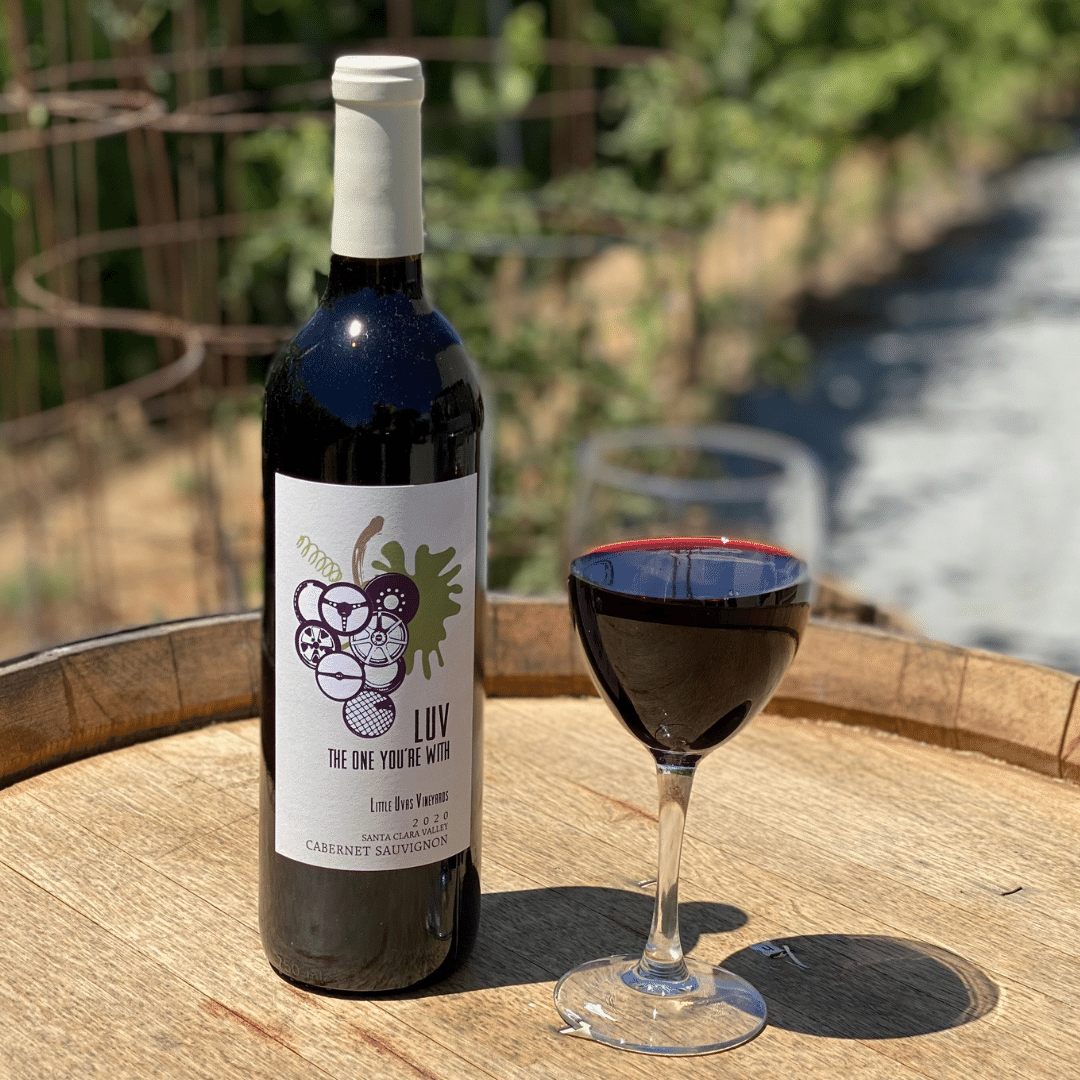 bottle of LUV's cabernet with a glass of the red wine on a wine barrel in the sun
