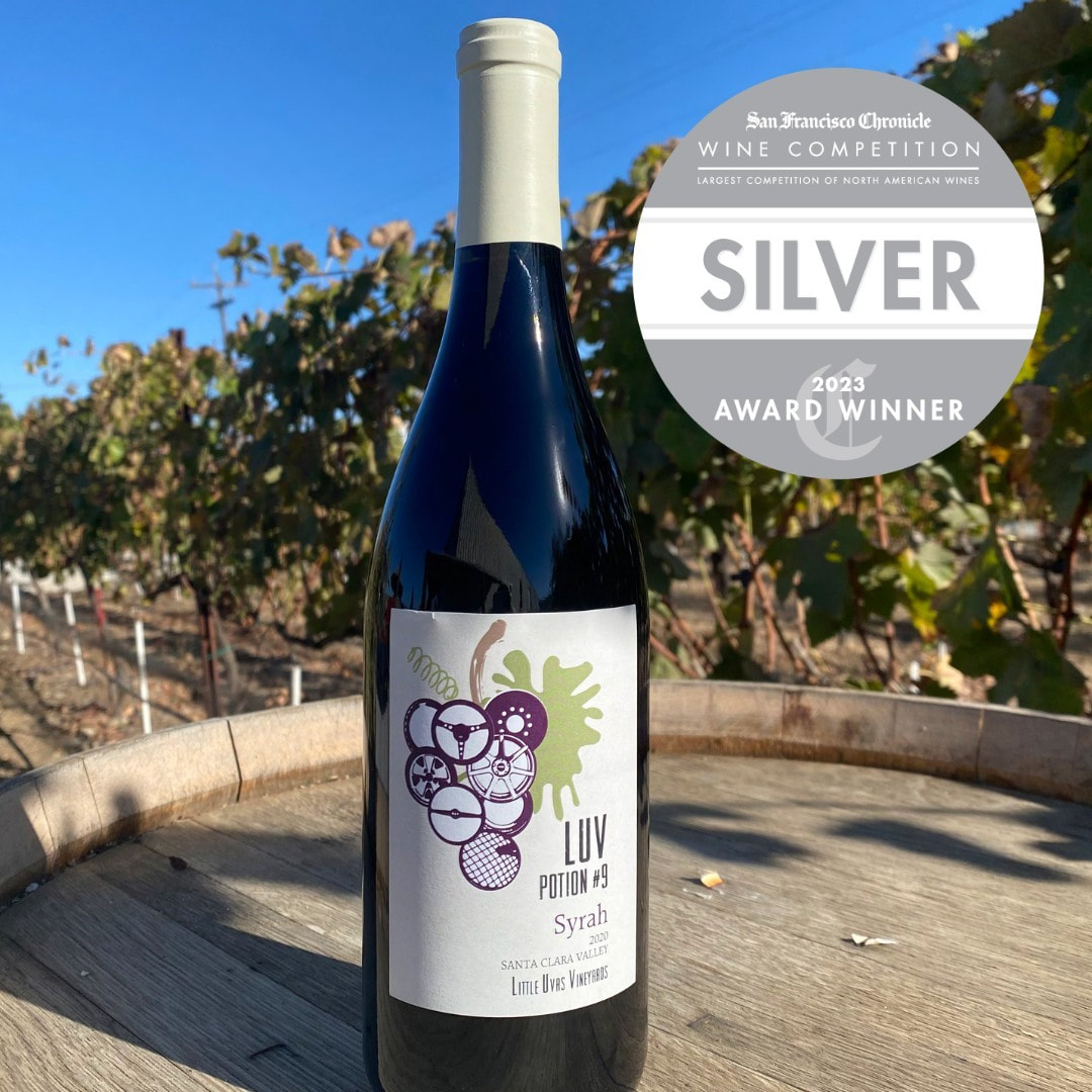 bottle of LUV Syrah on a wine barrel with silver award badge and vineyard in background